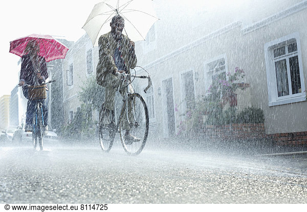 Couple with umbrellas riding bicycles in rain