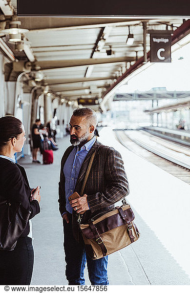Coworkers talking while standing at railroad station platform during business travel
