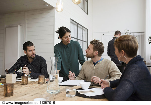 Coworkers talking with businesswoman at table in meeting