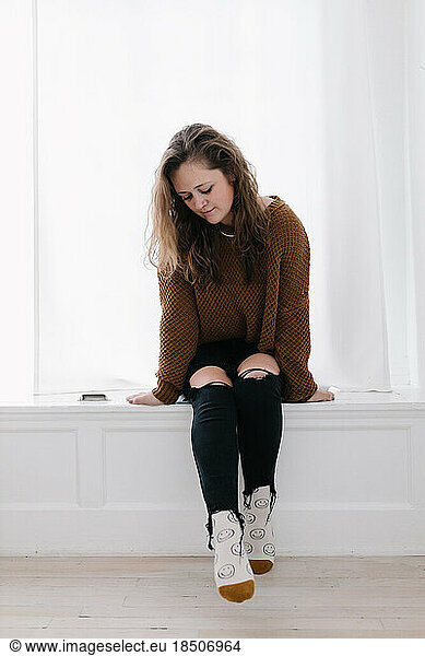 Cozy grown white woman in knit sweater and smiley socks in window seat