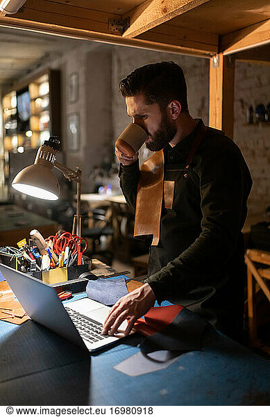 Craftsman drinking hot beverage and using laptop