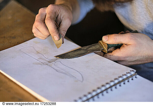 Craftsman holding knife on sketch pad at workshop
