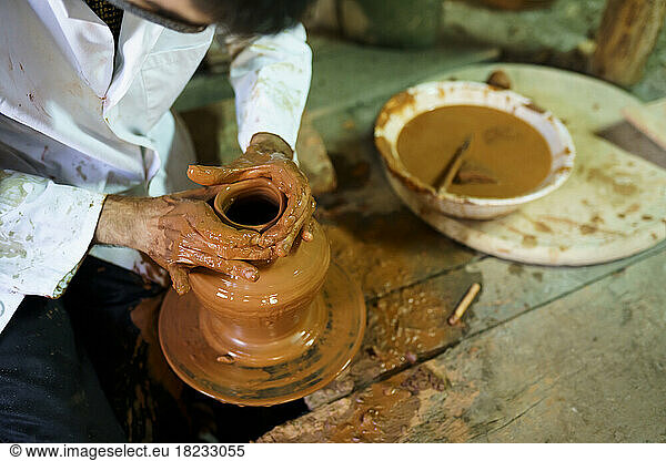 Craftsman molding pot on pottery wheel in factory