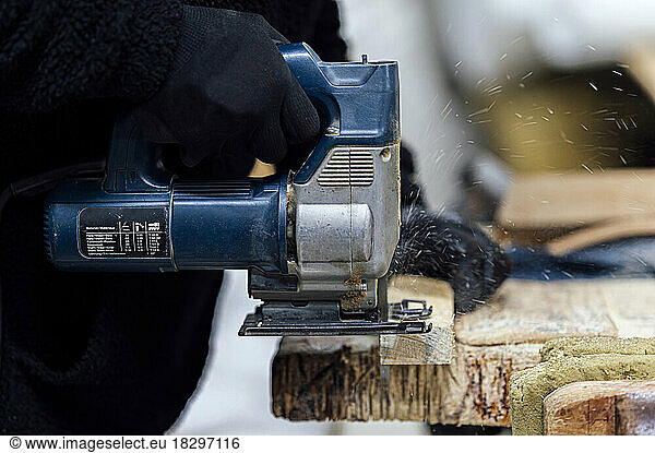 Craftsman using hand saw for cutting wood in workshop