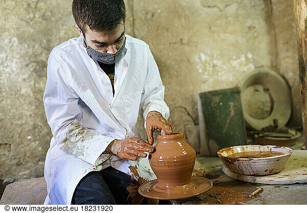 Craftsman wearing protective mask making pot on pottery wheel