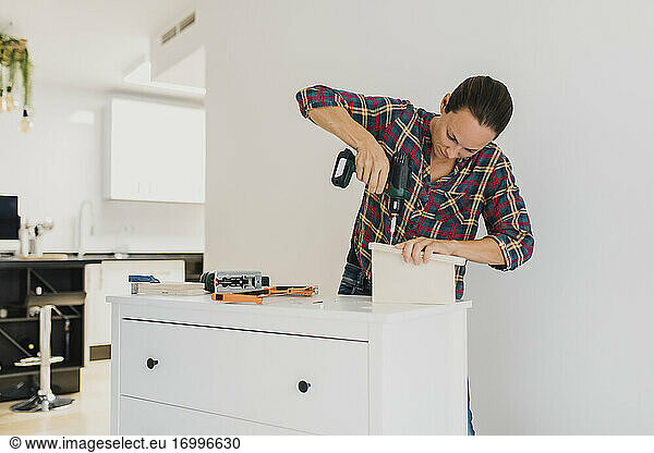 Craftsperson using electric screwdriver while standing by cabinet at home