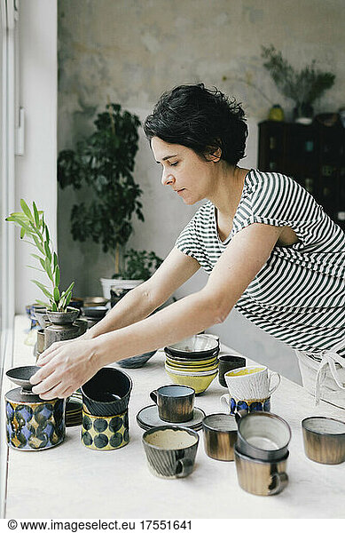 Craftswoman arranging crockery on table in ceramics store