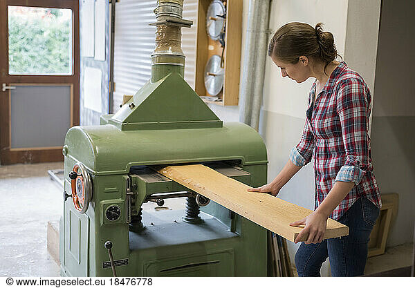 Craftswoman cutting plank through machine in woodshop