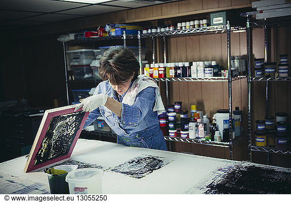Craftswoman examining ink prints on workbench at workshop