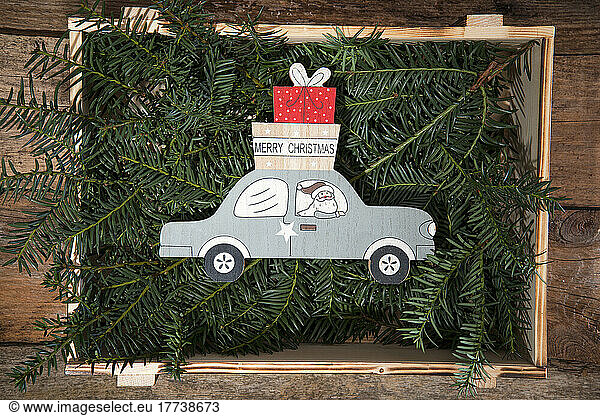 Crate filled with conifer twigs and Christmas decoration of Santa Claus delivering gifts by car