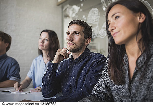 Creative business professionals listening while sitting in board room during meeting