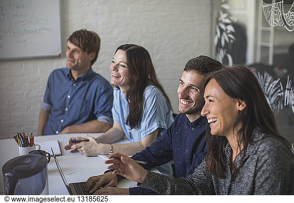 Creative business professionals smiling while sitting at conference table in board room