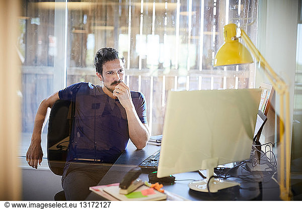 Creative businessman looking at computer monitor while sitting in office