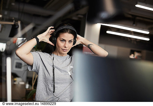 Creative businesswoman wearing headphones while looking at computer monitor in office