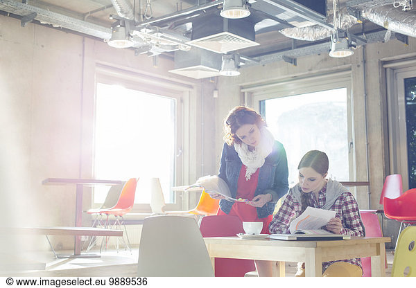 Creative businesswomen reviewing document edits in sunny office