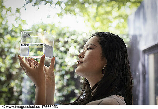 Creative female designer looking at cube with water at window