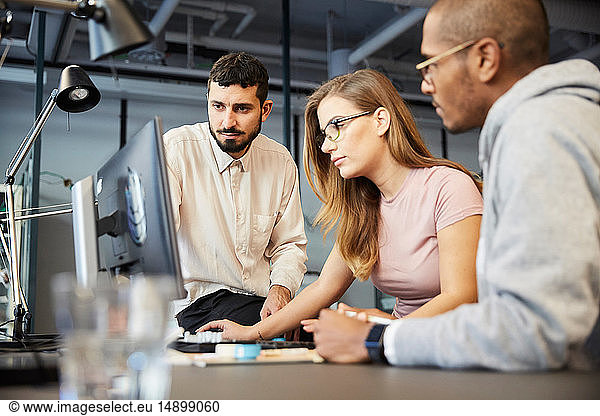 Creative male and female entrepreneurs looking at computer monitor during meeting in office