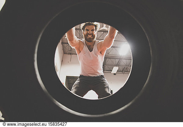 Creative view of strong man lifting large tire at gym