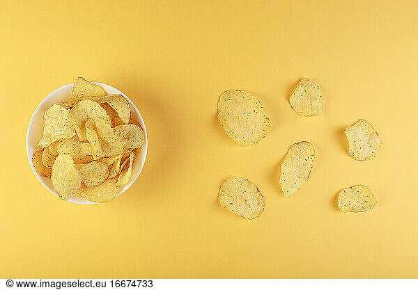 Crispy potato chips in bowl on yellow background  top view