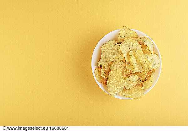 Crispy potato chips in bowl on yellow background  top view