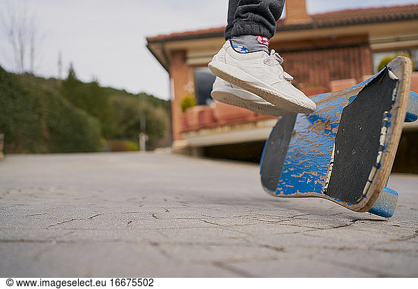 Crop kid in sneakers riding shabby skateboard on asphalt path