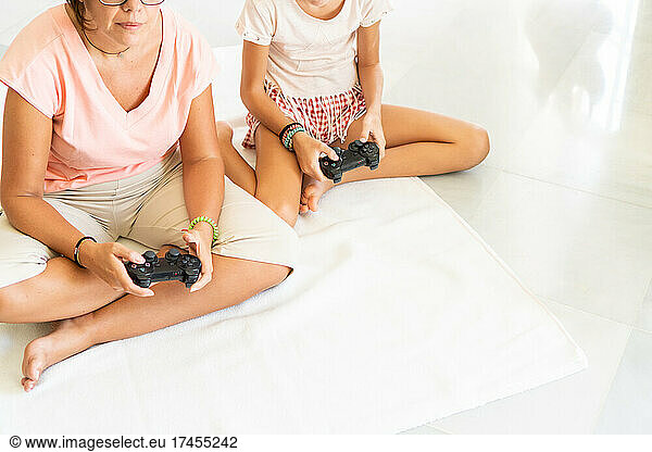 Crop mother and daughter playing video games together sitting on floor