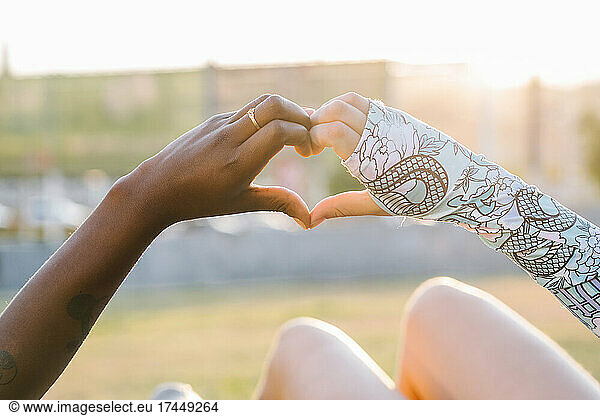 Crop multiracial girlfriends showing love gesture on meadow