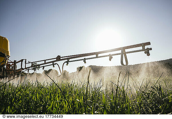Crop sprayer spraying fertilizer on field on sunny day