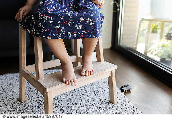 Crop view of little girl sitting barefoot on wooden step ladder
