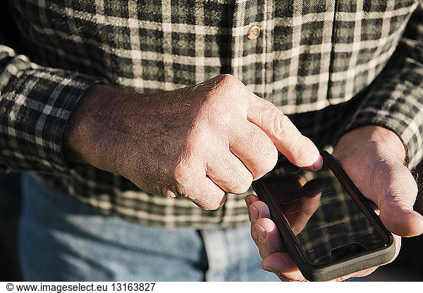 Cropped close up of senior male farmer using touchscreen on smartphone