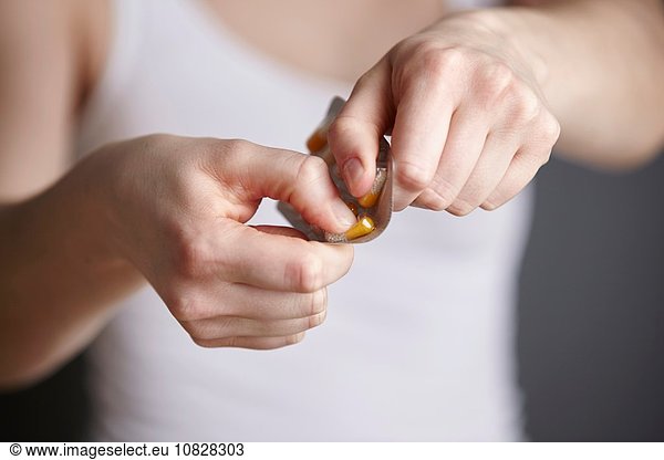 Cropped close up of young woman removing medicine capsule from blister pack