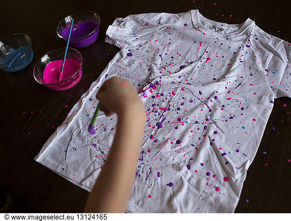 Cropped hand of girl splattering paint on t-shirt at home