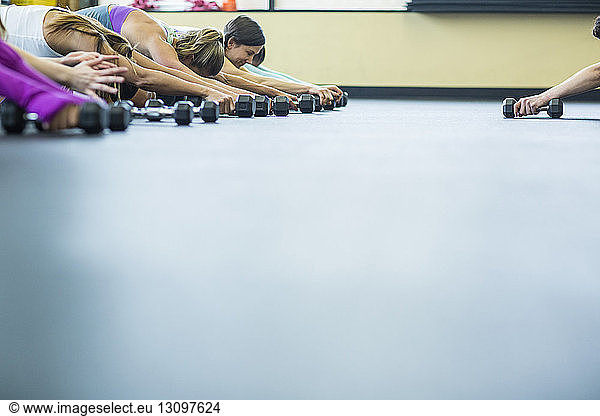 Cropped hand of instructor guiding women in exercising with dumbbells at gym
