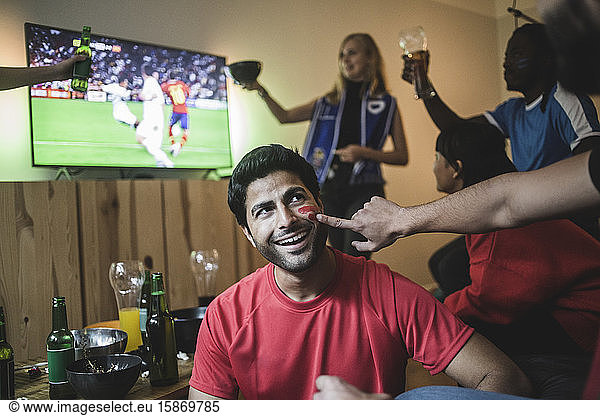 Cropped hand of man applying face paint on friend's cheek during soccer match