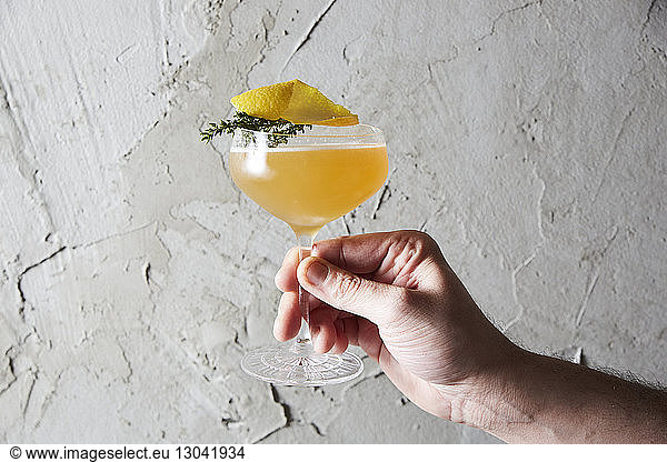 Cropped hand of man holding cocktail against wall