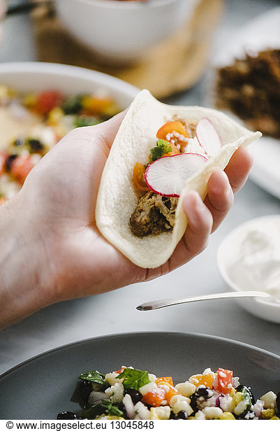 Cropped hand of man holding taco at dining table