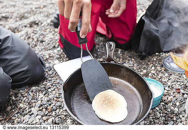 Cropped hand of man preparing pancake on cooking pan while camping outdoors