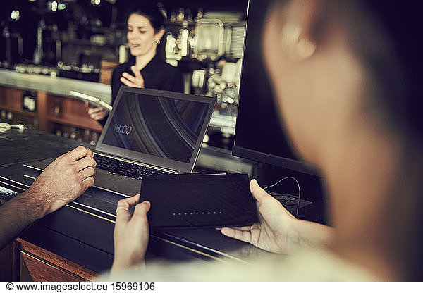 Cropped hand of man using laptop while woman holding modem in cafe