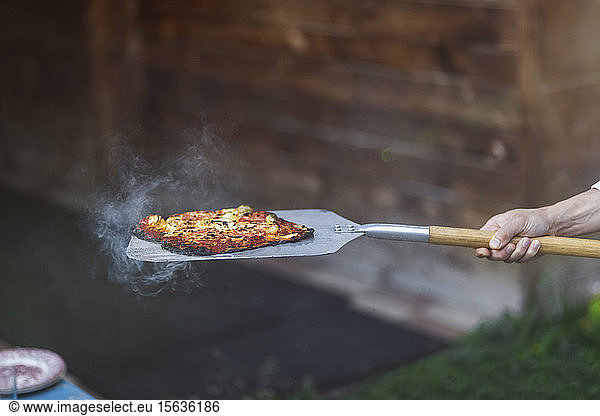 Cropped hand of person holding steamed pizza with spatula at summer party