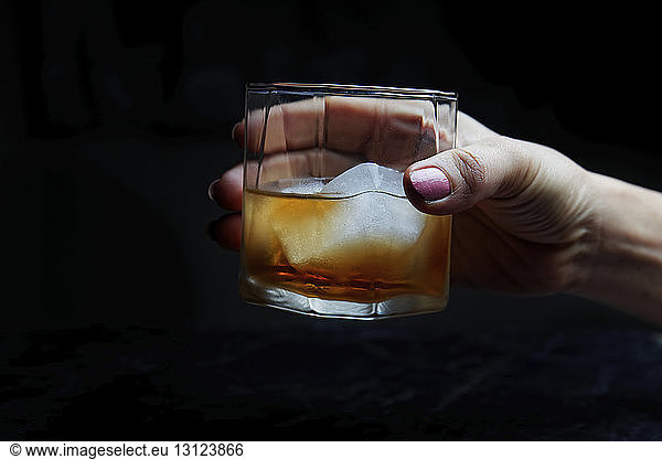 Cropped hand of woman holding alcoholic drink against black background