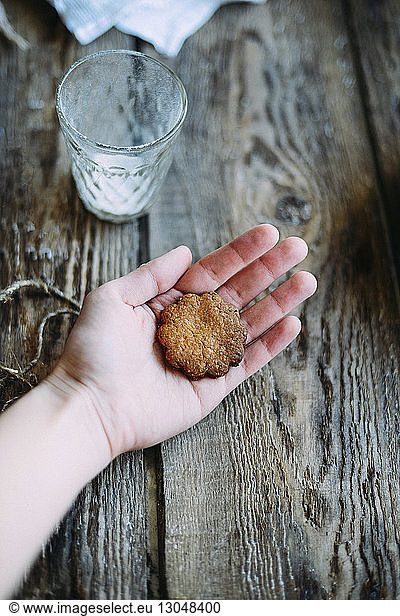 Cropped hand of woman holding gingerbread cookie by drinking glass on wooden table