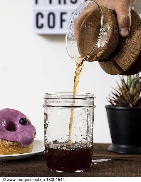 Cropped hand of woman pouring drink in mason jar by donut on table at home