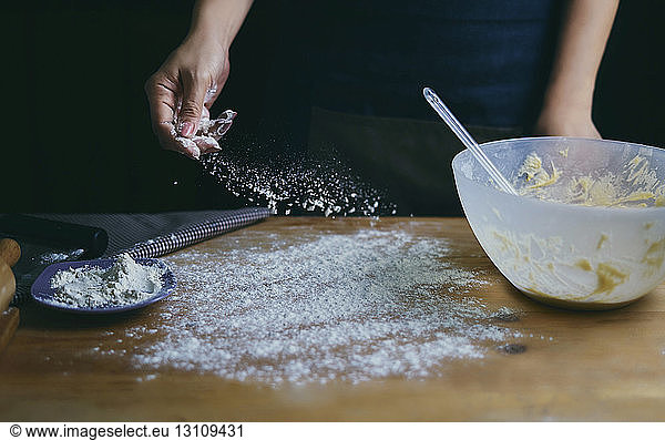 Cropped hand of woman sprinkling flour at kitchen counter