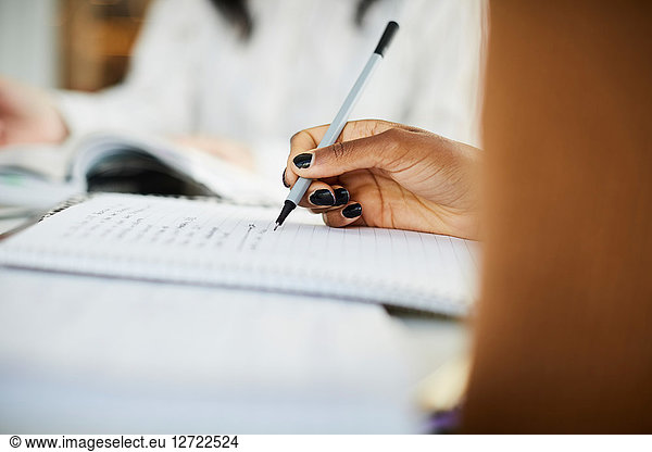 Cropped hand of woman writing on book while studying at table
