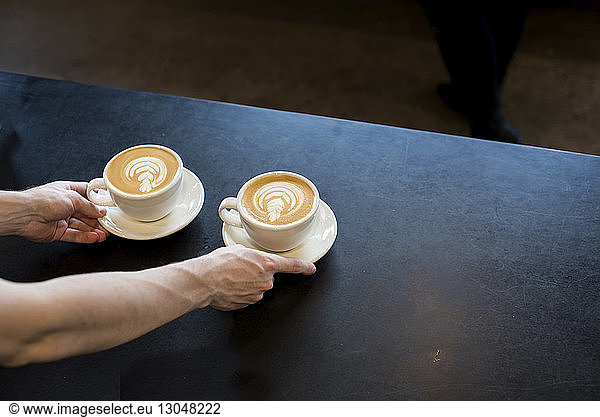 Cropped hands of barista serving frothy drinks on table at cafe
