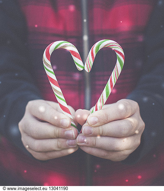 Cropped hands of boy holding candy canes during snowfall