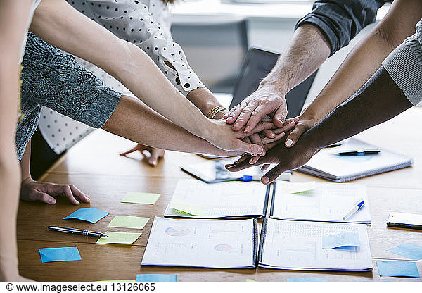 Cropped hands of business people huddling in meeting at board room