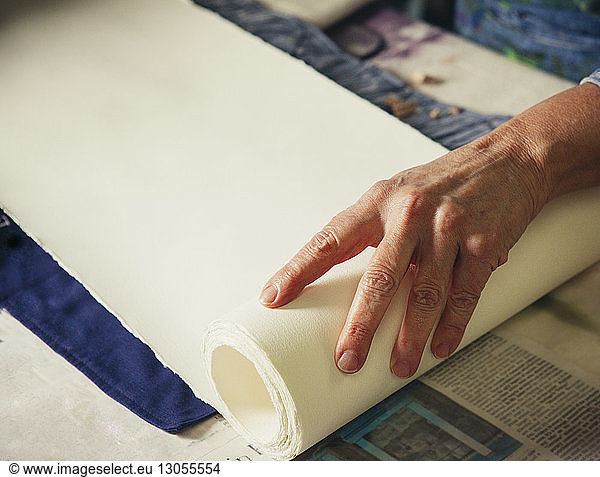 Cropped hands of craftswoman adjusting rolled up paper on fabric at workshop