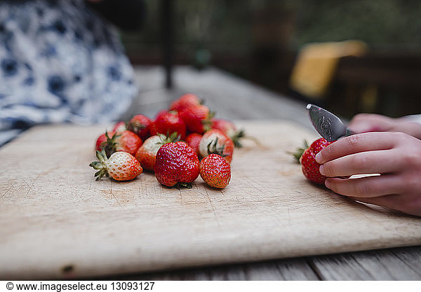 Cropped hands of girl cutting strawberry on cutting board at table