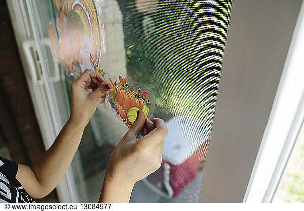 Cropped hands of girl sticking fruits label on window glass at home